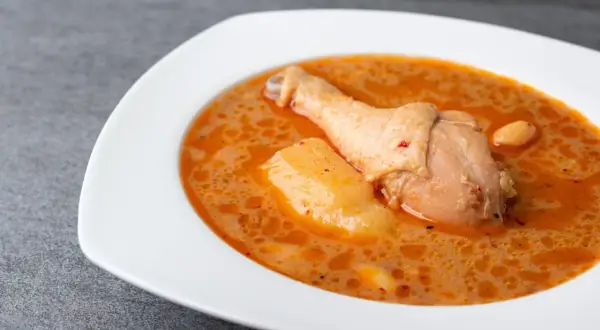 En vit skål med en kycklingklubba och potatis i en krämig, kryddig sås. En härlig chicken massaman.