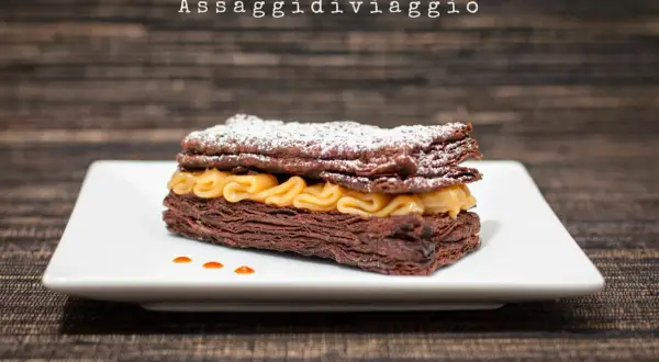 Un goloso millefoglie al cioccolato, con strati croccanti e crema dorata, spolverato di zucchero a velo.