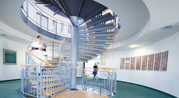 Moderne Wendeltreppe in einer Klinik mit zwei Personen, die sie benutzen.