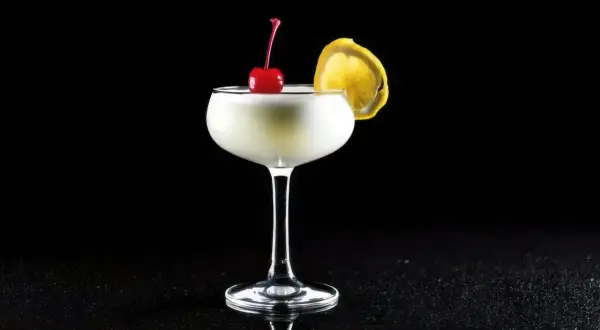 En elegant drink, en "white lady", med körsbär och citronskiva på svart bakgrund.