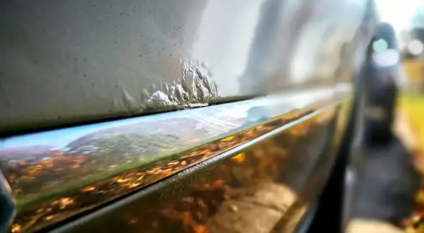 Nahaufnahme von Rostblasen am Auto, die eine Rostbehandlung am Auto erfordern.