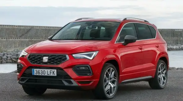 Czerwony Seat Ateca z nowoczesnymi światłami LED stoi na tle kamiennego nabrzeża i spokojnej wody.