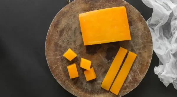 Un bloque de queso color naranja, cortado en cubos y bastones, sobre una tabla de madera.