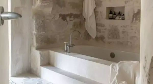 Une **salle de bain méditerranéenne** avec baignoire en pierre brute, robinetterie moderne et serviette blanche suspendue.