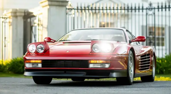 Czerwone Ferrari Testarossa z podnoszonymi światłami, zaparkowane przed elegancką posiadłością.