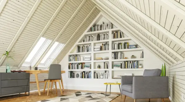 Gemütlicher Arbeitsplatz mit Bücherregalen im Dachausbau. Ein Schreibtisch unter Dachfenstern und eine Leseecke laden zum Verweilen ein.