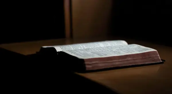 Otwarta Biblia leżąca na drewnianym stole, oświetlona od góry.