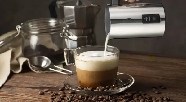 En hand häller mjölkskum i en kaffekopp, redo för ett perfekt kaffe recept. Kaffebönor sprider sig över träbordet.