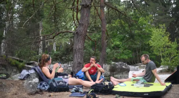Drei Kletterer machen eine Pause im Wald von Fontainebleau. Ein Mann isst, während die anderen sich ausruhen.