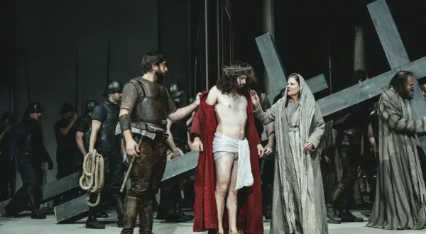 Szene aus einem Passionsspiel: Jesus mit Dornenkrone, umgeben von Soldaten und Frauen, die ein Kreuz tragen.