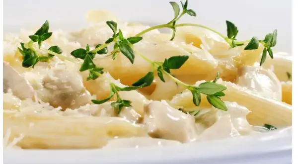 Penne z kurczakiem w kremowym sosie jogurtowym, posypane parmezanem i udekorowane gałązkami tymianku.
