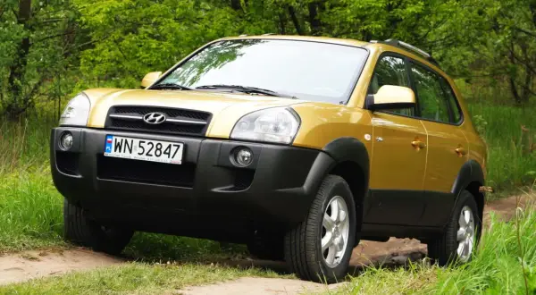 Złoty Hyundai Tucson 2007 na leśnej drodze, gotowy na przygodę.