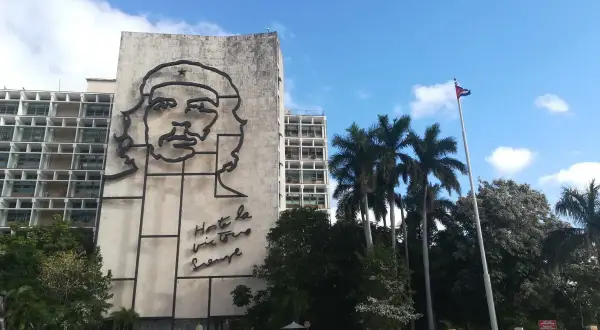 Monumentalny portret Che Guevary zdobi budynek w Hawanie, stolicy Kuby. Obok palm i kubańska flaga.