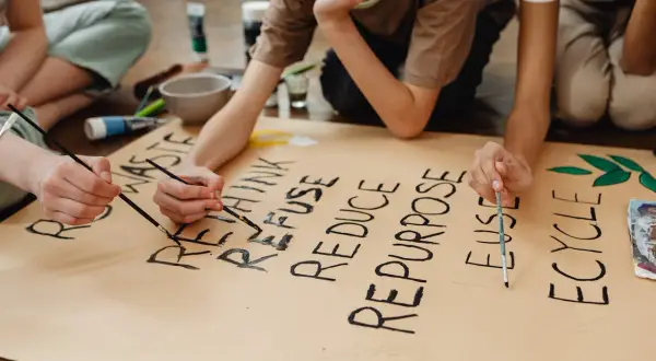 Niños pintan un cartel sobre la **competencia ciudadana LOMCE** y el reciclaje: "RETHINK, REFUSE, REDUCE, REPURPOSE, REUSE, RECYCLE".