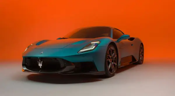 Niebieski Maserati MC20 z charakterystycznym logo na grillu, prezentowany na tle pomarańczowego gradientu.