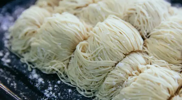 Des portions de pâtes crues, fines et blanches, sont disposées sur un plateau. Une question se pose : peut-on congeler des pâtes cuites ?