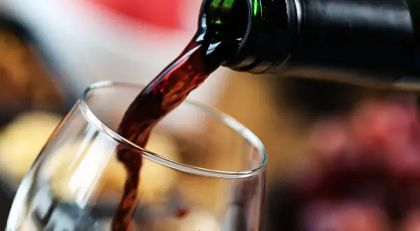 Mętne wino leje się z butelki do kieliszka. Ciemny płyn tworzy wiry, zapowiadając bogaty smak.