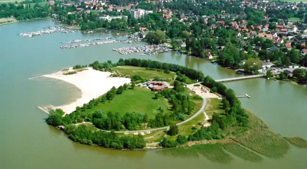 Grüne Insel mit Sandstrand und Gebäuden im Steinhuder Meer, umgeben von einem Yachthafen und einer Ortschaft.