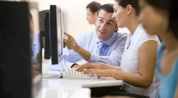 Uomo indica schermo a collega, mentre lei digita. Un tirocinio extracurriculare con stipendio è un'ottima opportunità.