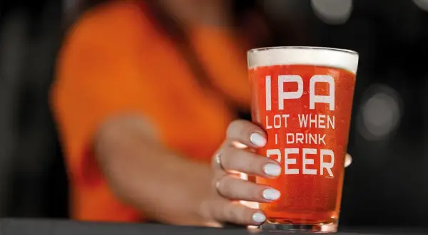Un bicchiere di IPA con la scritta "IPA LOT WHEN I DRINK BEER" tenuto da una mano con unghie bianche.