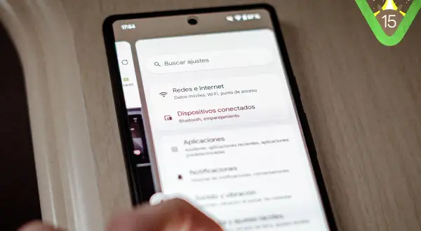 Mano interactuando con un teléfono que muestra la configuración de Android 15. El logo de Android 15 aparece en la esquina superior derecha.