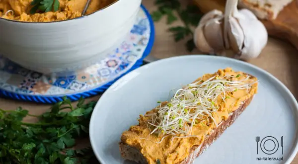 Pyszna pasta z kurczaka na kromce chleba, posypana kiełkami. Obok miska z pastą, czosnek i natka pietruszki.