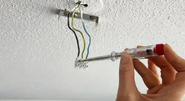 Hand mit Schraubendreher prüft Kabel für die Montage einer Lampe an der Decke.