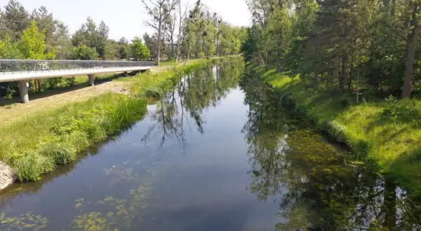 Piękny dzień na odkrywanie tras rowerowych w Bydgoszczy. Mostek nad kanałem, otoczony zielenią, zaprasza do przejażdżki.