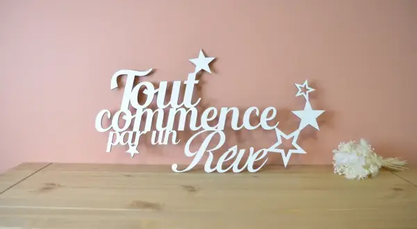 Une **lettre en bois blanc** forme la phrase "Tout commence par un Rêve", ornée d'étoiles. Un petit bouquet de fleurs séchées est posé à droite.
