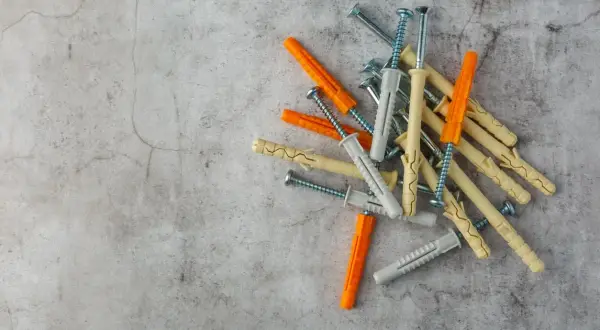 Montón de tacos de pared de plástico y tornillos. Hay varios tipos de tacos de pared, de colores naranja, gris y beige, listos para fijar objetos.