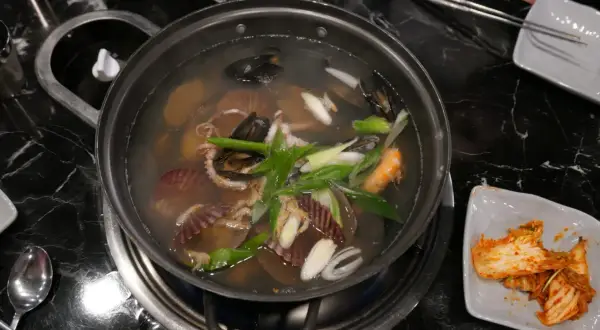 Un plat de cuisson de fruits de mer mijote dans un bouillon, avec des moules, des crevettes, des pétoncles et des poulpes.