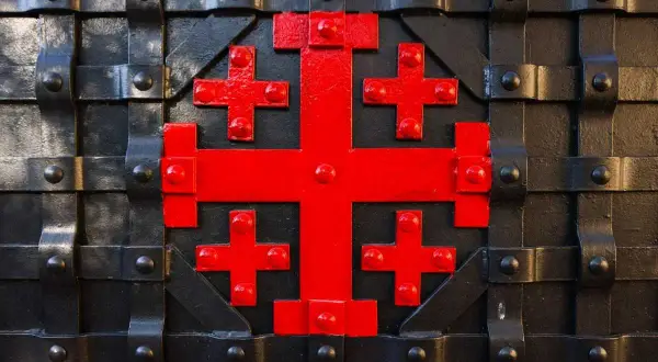 Czerwony krzyż jerozolimski znaczenie symbolizuje pięć ran Chrystusa, ozdabia czarną, metalową bramę.