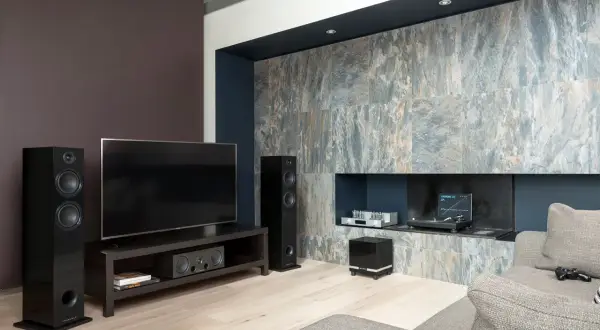 Nowoczesny salon z telewizorem, głośnikami i czarnym subwooferem. To właśnie subwoofer co to, urządzenie wzmacniające niskie tony.