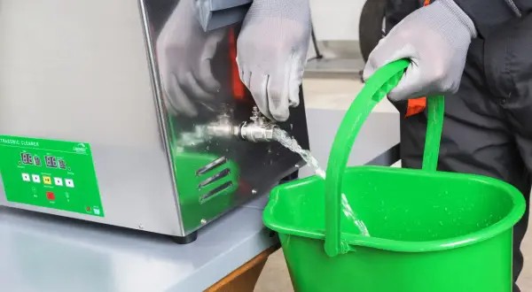 Opróżnianie myjki ultradźwiękowej. Woda wypływa z zaworu do zielonego wiadra.