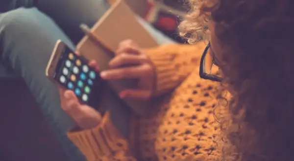 Kobieta z burzą loków i okularami na nosie przegląda aplikacje na telefonie, ucząc się, jak pobierać aplikacje na iPhone.