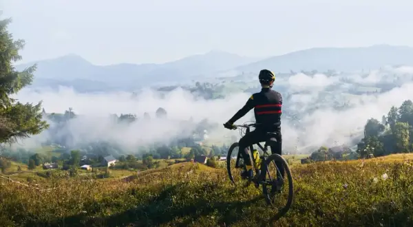 Rowerzysta podziwia mglisty krajobraz dolnośląskiej krainy rowerowej. W oddali góry i malownicze wioski.