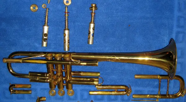 Rozłożona trąbka, instrument dęty blaszany, leży na niebieskim tle. Widać jej poszczególne części: korpus, wentyle, ustnik i inne elementy.