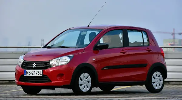 Czerwony Suzuki Celerio z kierowcą za kierownicą, zaparkowany na zewnątrz.