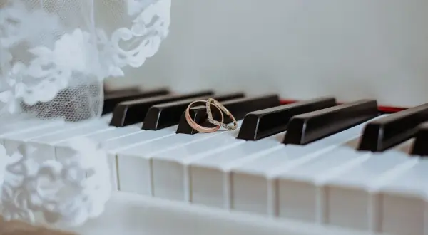 Dwa obrączki na klawiszach pianina, obok białej koronki. Gotowa lista utworów do ZAIKS wesele.