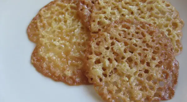 Tre gyllene havreflarn utan sirap ligger på en vit tallrik. De är tunna och krispiga med ett vackert nätmönster.