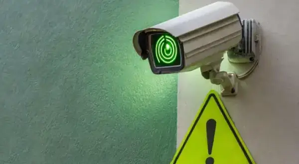 Caméra de vidéosurveillance allumée, prête pour la maintenance. Un panneau de signalisation jaune avec un point d'exclamation est visible à proximité.
