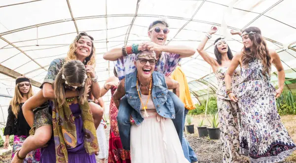 Grupa przyjaciół w stylu hippie świętuje w szklarni, śmiejąc się i bawiąc.