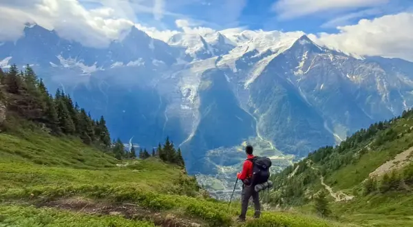 Randonneur contemplant les majestueuses montagnes enneigées, un paysage digne des **Vosges** en été.