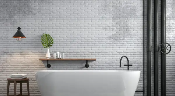 Bagno moderno con vasca bianca, mattoni a vista e tubi industriali neri. Ottime idee per coprire tubi a vista con stile.