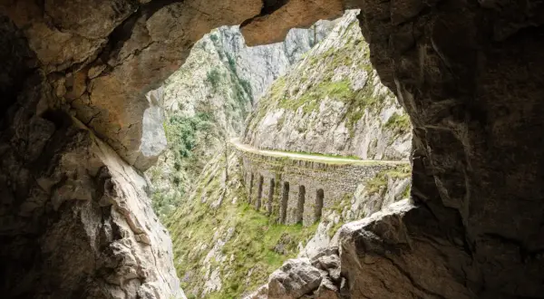 Vista desde una cueva de la ruta del Cares, con un camino tallado en la roca y arcos de piedra.