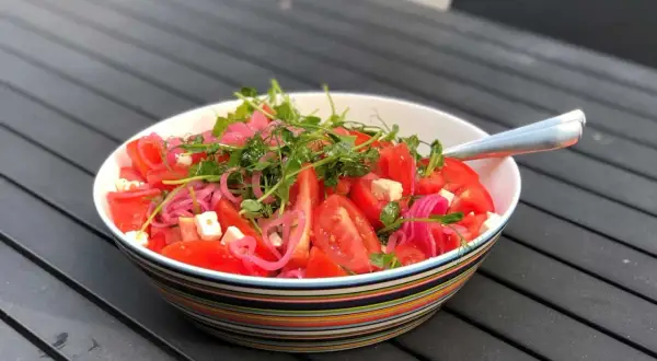 En skål med en färgglad tomatsallad med fetaost, rödlök och groddar. En god sallad till maten som ser fräsch och inbjudande ut.
