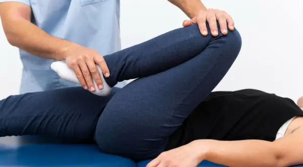 Fizjoterapeuta wykonuje ćwiczenia z pacjentem, którego noga jest zgięta w kolanie. To część terapii, która może pomóc w leczeniu zespołu sudeckiego.
