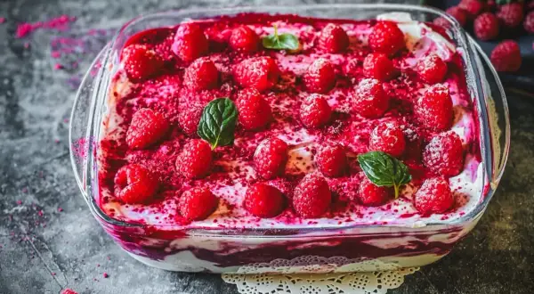 Himbeer Tiramisu in einer Glasform, garniert mit frischen Himbeeren und Minzblättern. Ein süßer Genuss!