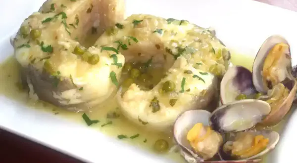 Congrio en salsa verde con guisantes y almejas, un plato delicioso y lleno de sabor.