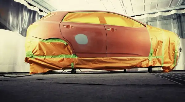 Auto in carrozzeria, pronta per verniciare con bomboletta. Finestrini e parti non interessate coperti con teli arancioni e nastro verde.